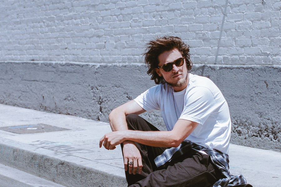 A man in a white tee sits on a sidewalk.