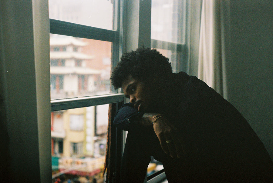 A man looks pensively out a window in a dark room