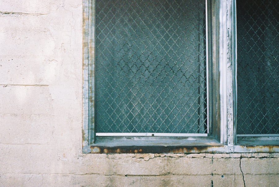 An old window with rusting sills on a whitewashed brick wall.