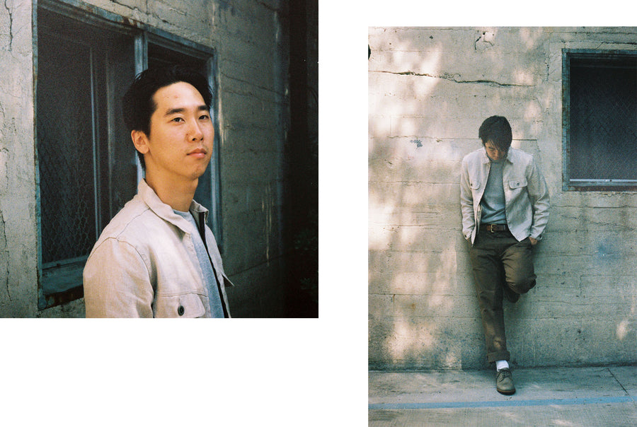 The model leans up against a wall with one leg up, showing off his entire outfit.