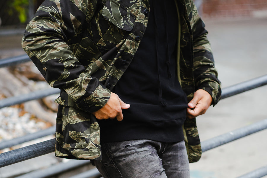 A close-up shot of a man in a camouflage jacket and beat-up black jeans.