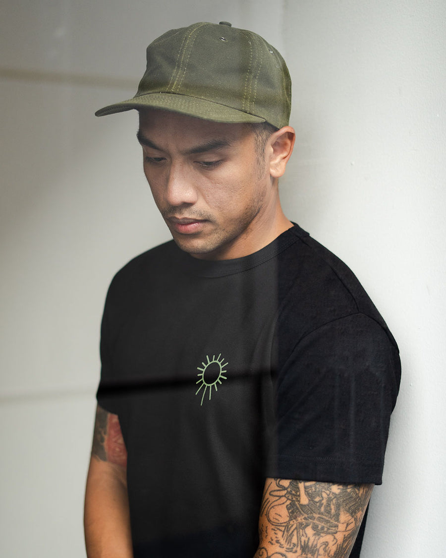A man in an olive hat and black tee looks down at the ground.