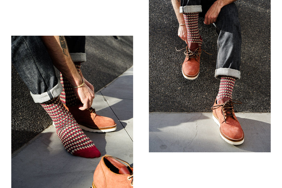 A man wearing red patterned socks puts on some Viberg oxfords.