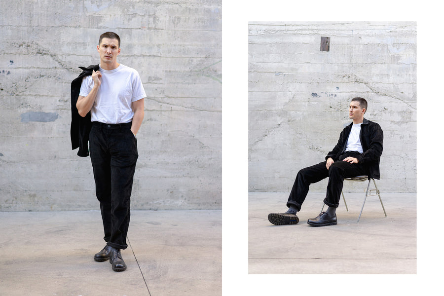 A young man looks into the camera with a black corduroy suit on.