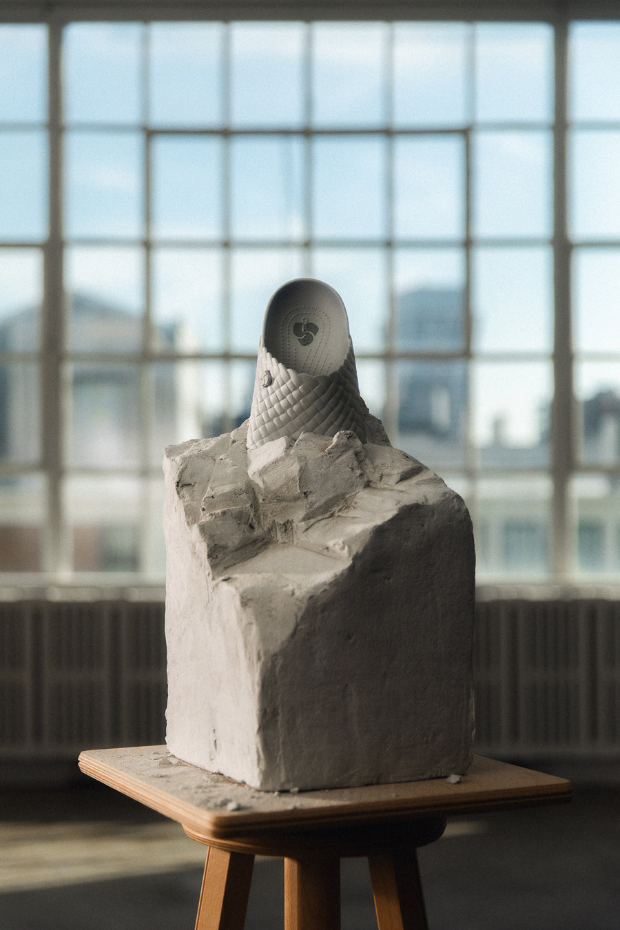 A grey clog embedded in a carved concrete block sits upon a wooden pedestal.