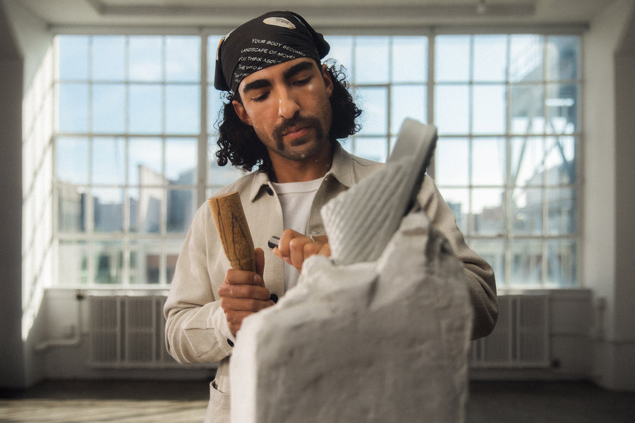 A man with a hammer and chisel carves a shoe out of a block of stone.
