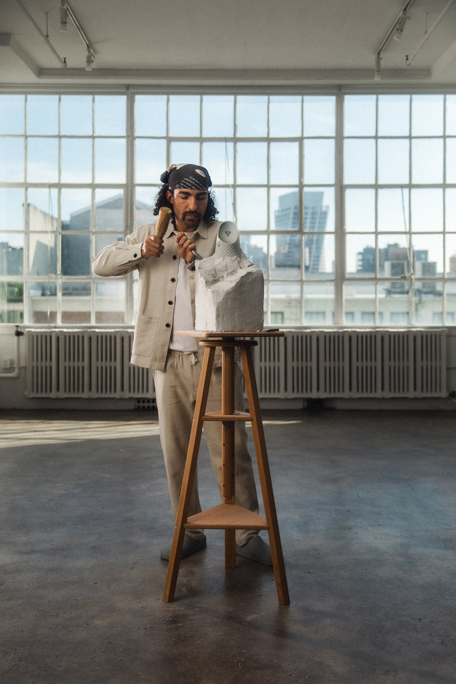 A man stands and carves a stone block in a big studio space.