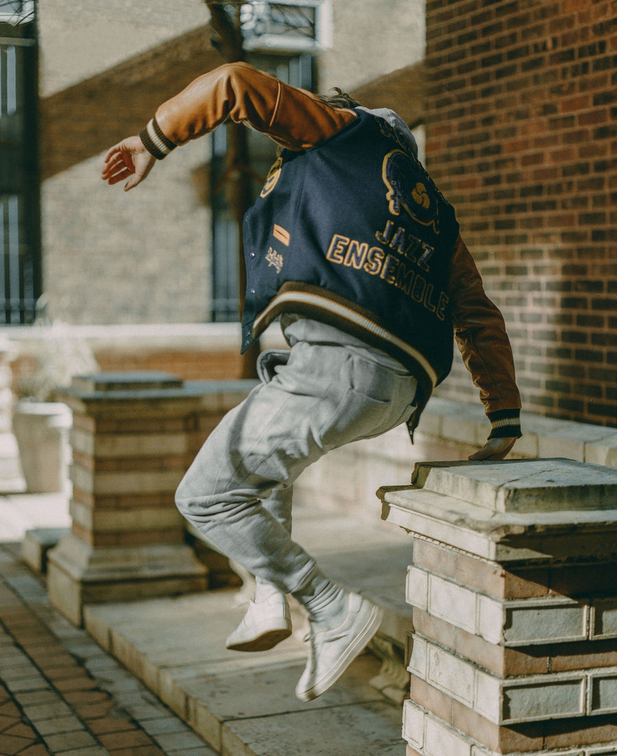 A man in a varsity jumps off a wall.