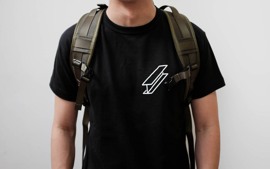 A model wears a black logo tshirt with an olive backpack on his back.