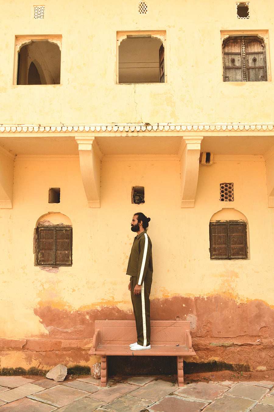 A man stands on a bench in a green track jacket and pants.