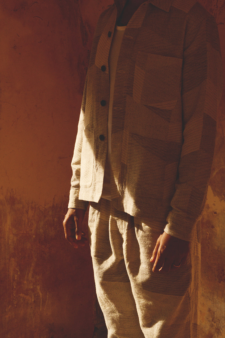 A man in a grey jacket and pants stands in a shadow with a beam of light slicing through.