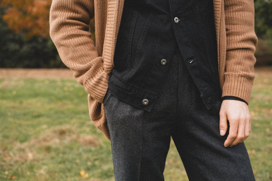 A detailed shot of a brown sweater worn over a black denim jacket and grey flannel pants.