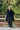 A man in a black wool coat stands on a bridge.