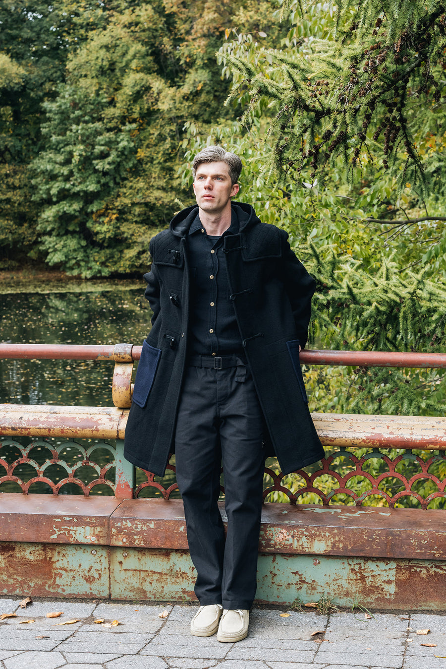 A man in a black wool coat stands on a bridge.