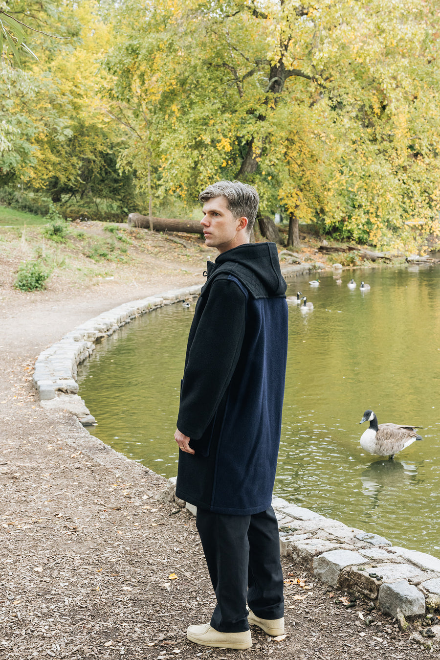 A man stands by a lake with ducks.