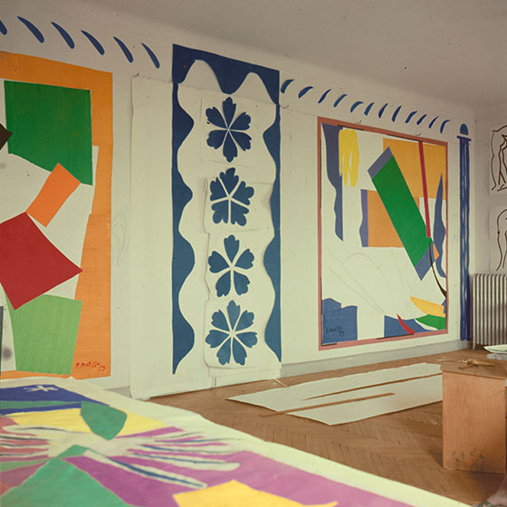 A photo of Matisse's studio with large pieces of artwork taped to a wall.