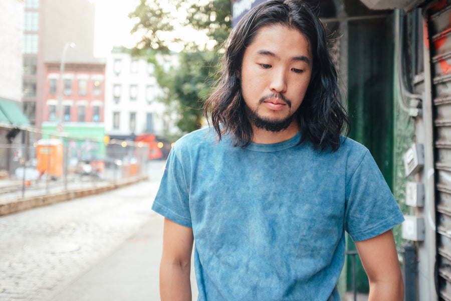 A portrait of a man wearing a light crumple dye indigo tshirt.