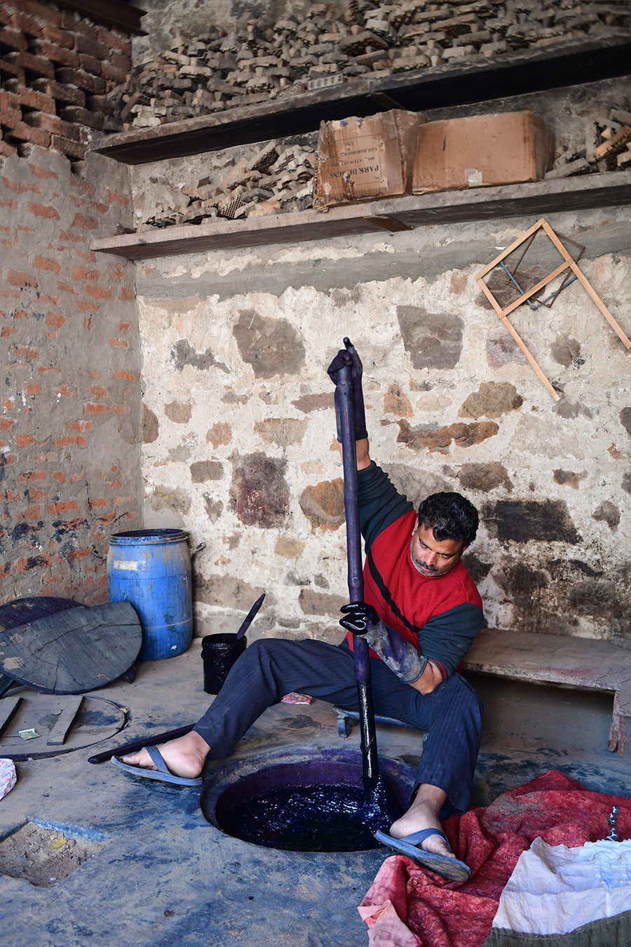 A man stirs garments in an indigo vat with a long wooden pole.