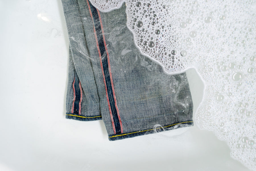 A pair of 3sixteen jeans laying in a bathtub with laundry detergent.