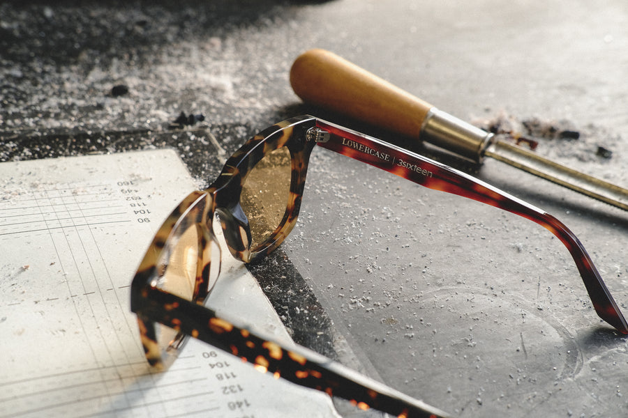 A pair of yellow-lens sunglasses sit completed on a dirty table.