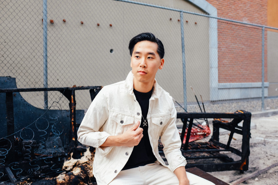 Model holds side panel of jacket in his right hand while looking off camera.