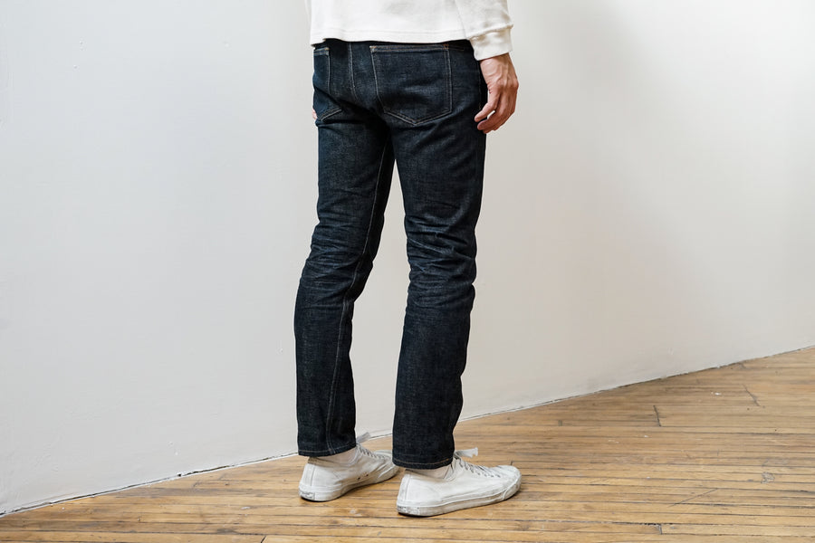 The model stands still facing away from the camera, showing the back pockets and the honeycombs forming on the backside of the jeans.