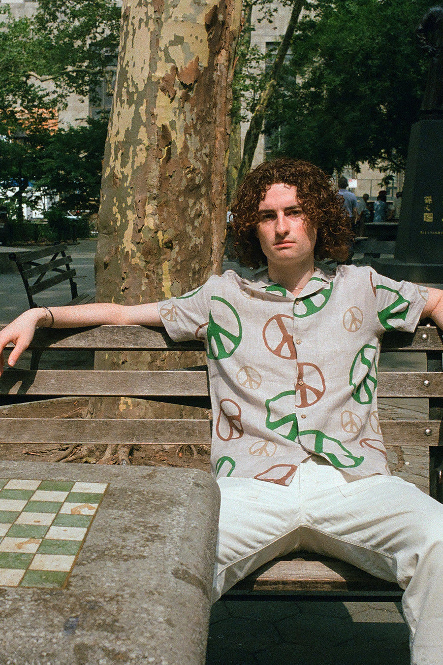 A man in a colorful peace shirt sits on a park bench.