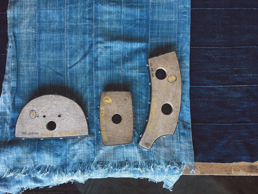 Hat molds, used to cut fabric into specific shapes, lay on top of the indigo blankets.