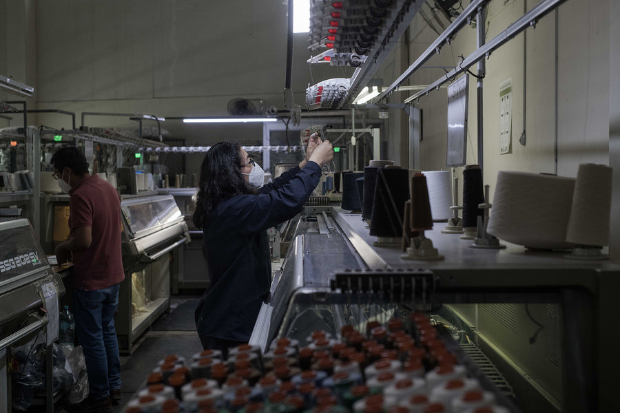 Two people work on a knitting machine.