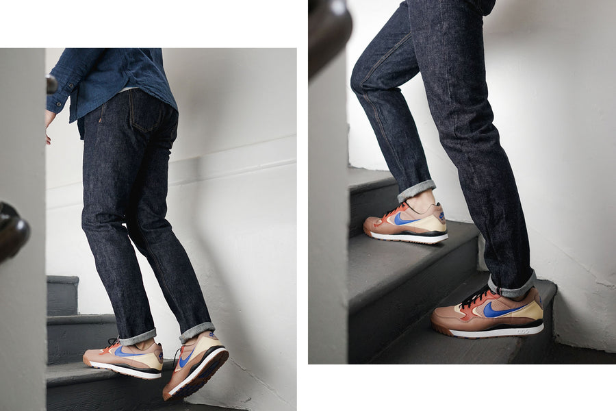 The model walks up a flight of stairs wearing a blue chambray and indigo rinsed Kibata jeans by 3sixteen.