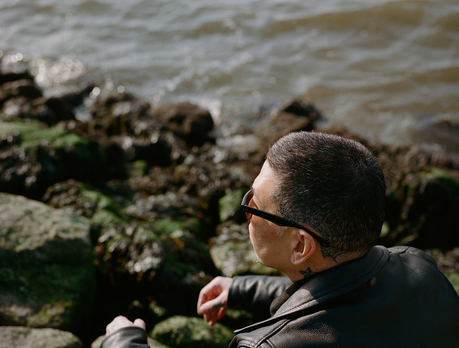 A man sits on mossy rocks by the water.