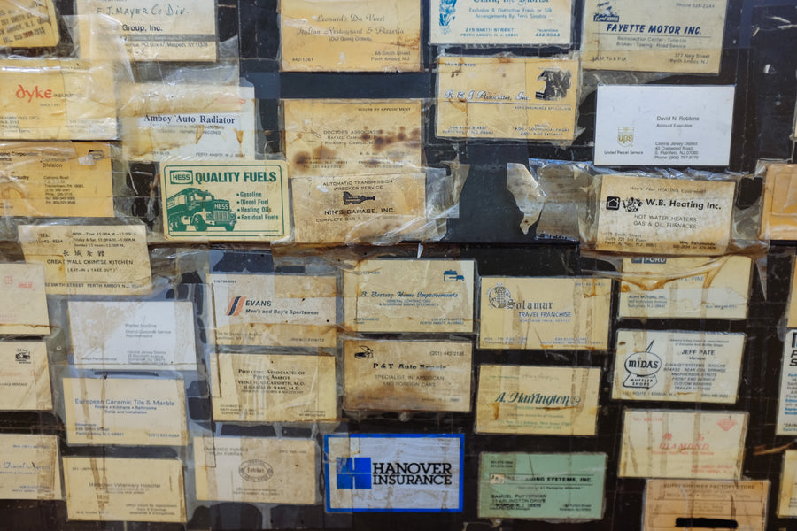 Various old business cards accumulated over decades are taped onto an old metal desk.
