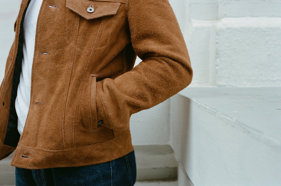 A closeup photo of a tan suede leather jacket with the wearer's arm in the side pocket.