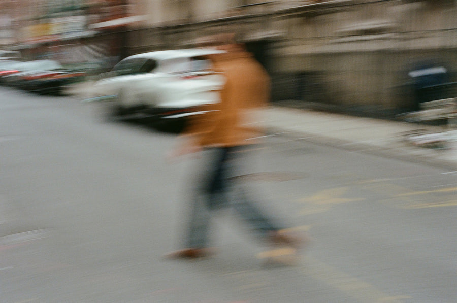 A blurry photo of a man in a suede jacket crossing the street