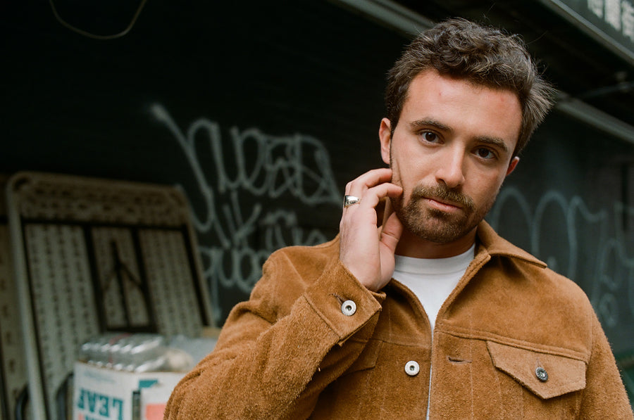 A portrait of a man in a suede jacket touching his face.