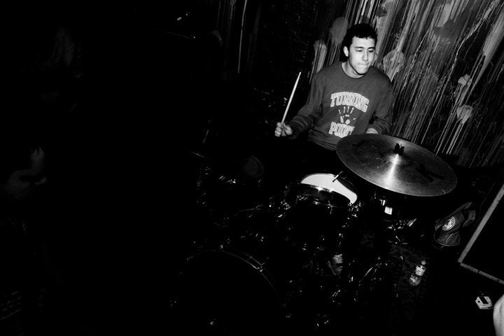 A black and white photo of Spencer playing the drums in a hardcore band.
