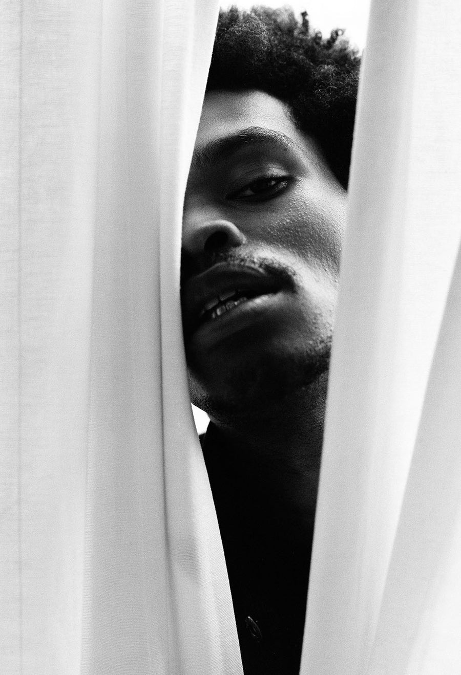 The model's face peers out from between two white drifting curtains.