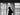 A silhouette of a model standing in front of two curtains blowing in the wind.