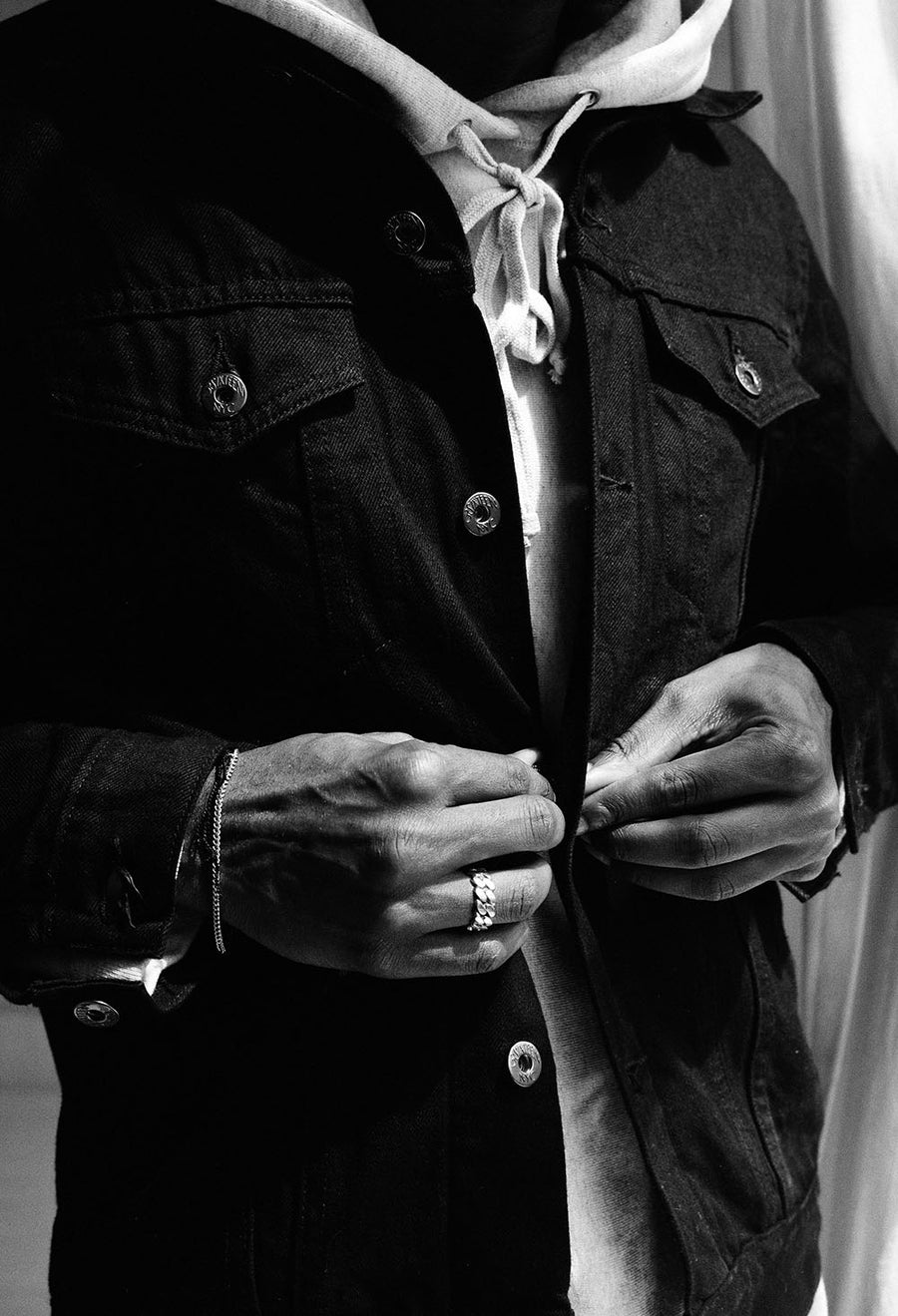 A detail shot of the model buttoning up a 3sixteen denim jacket with both hands. 