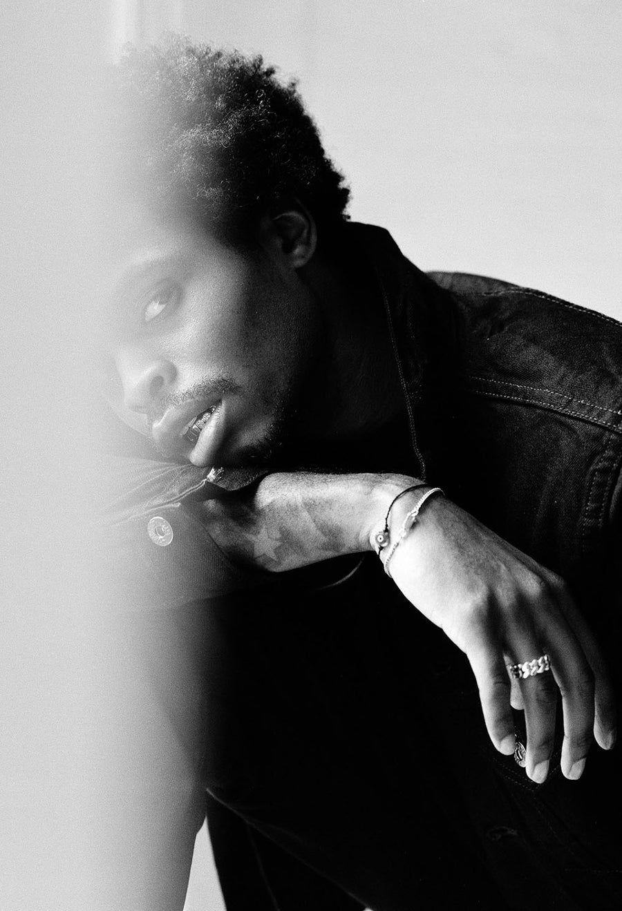 An artful photo of a model leaning over his forearm, looking into the camera wearing a 3sixteen denim jacket.