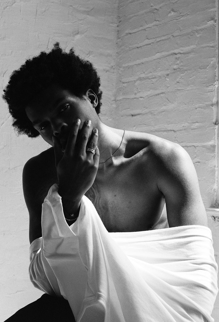 The model stares into the camera with his white tee half-removed, hand over mouth.