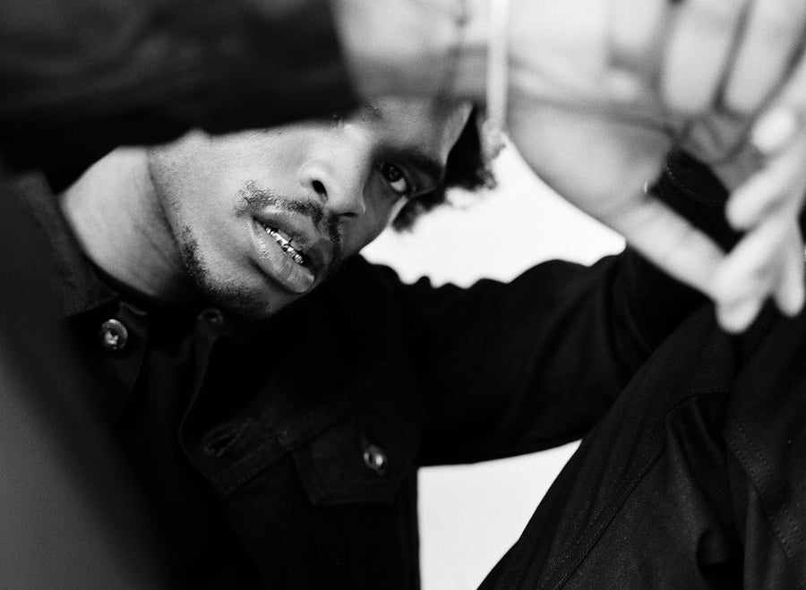 A closeup shot of the model as he gazes fiercely into the camera with arms draped over his knees. 