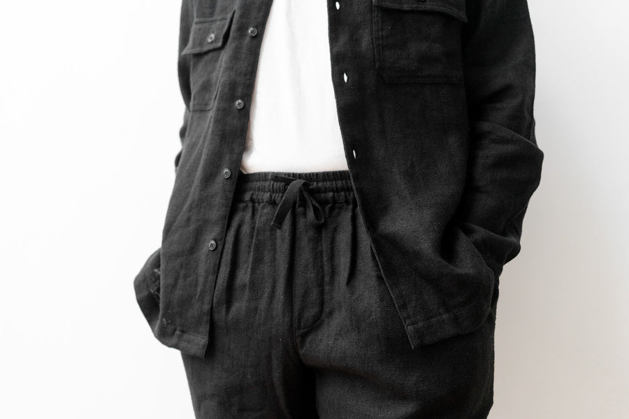 A shot of the elastic waist of a pair of black linen pants with a white tee tucked in.