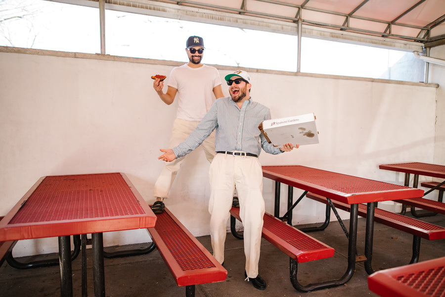 Two dirtbags eat pizza amongst a lot of red picnic tables.