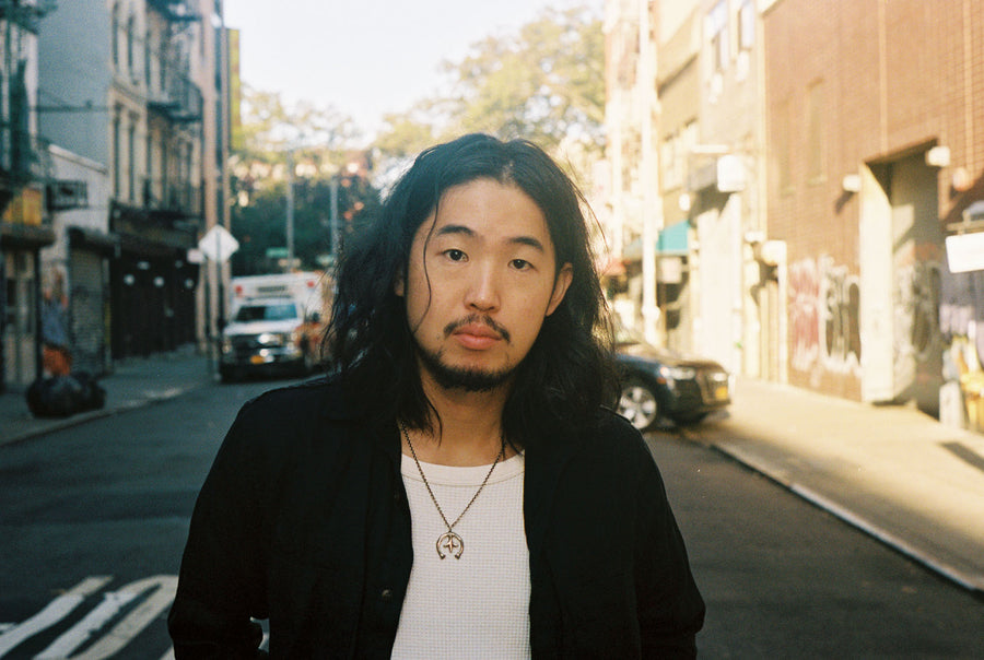 A portrait of the model standing in the middle of a street wearing a black 3sixteen shirt and a silver necklace.