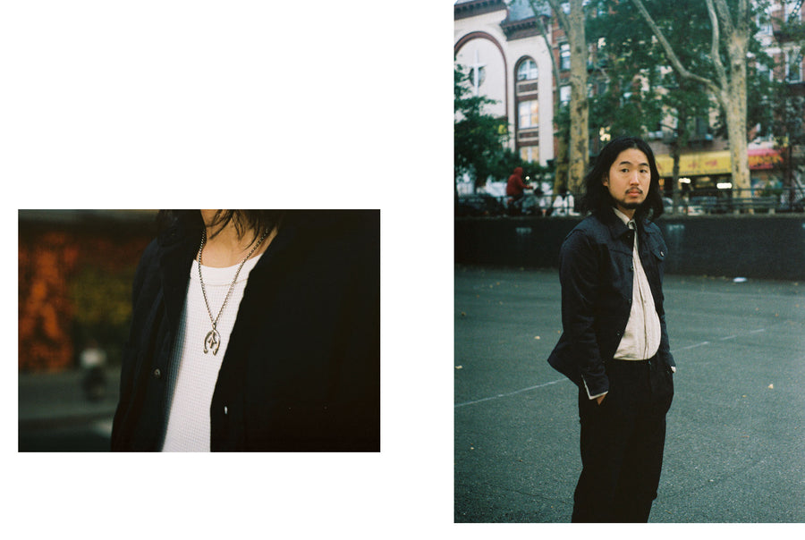 The model stands in the middle of a playground court wearing a Ranch Jacket, natural linen shirt, and black pants.