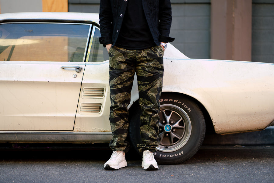 Bottoms-only shot of the camouflage pants stacked on some white Viberg sneakers.