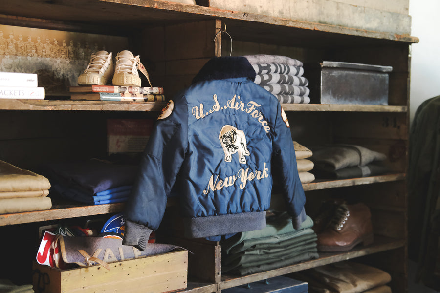A kids souvenir jacket in a blue satin hangs on a shelf.