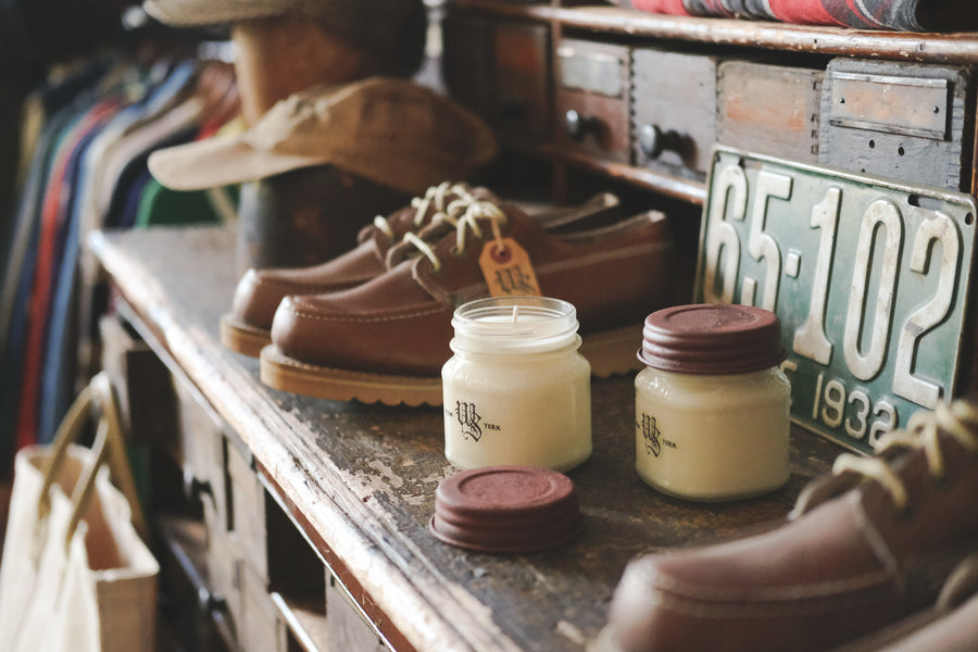 An old wooden shelf with candles, shoes and other ephemera on it.